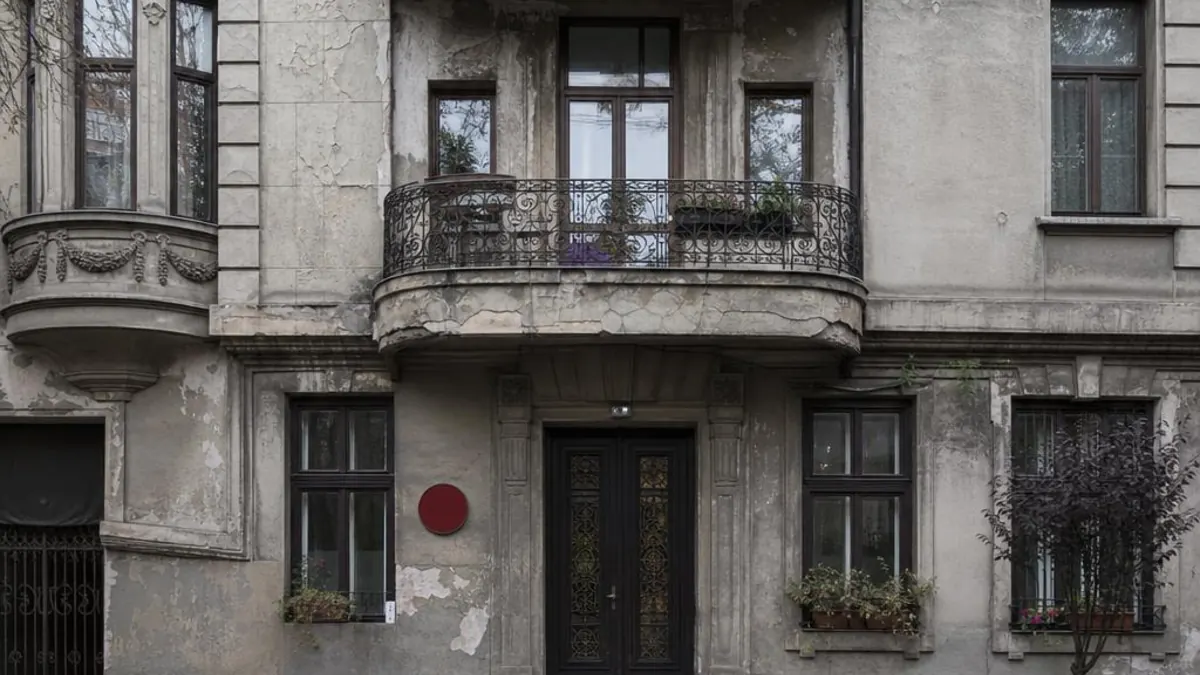 Fațada unei clădiri vechi din București cu balcon din fier forjat și bulină roșie de risc seismic lângă intrare